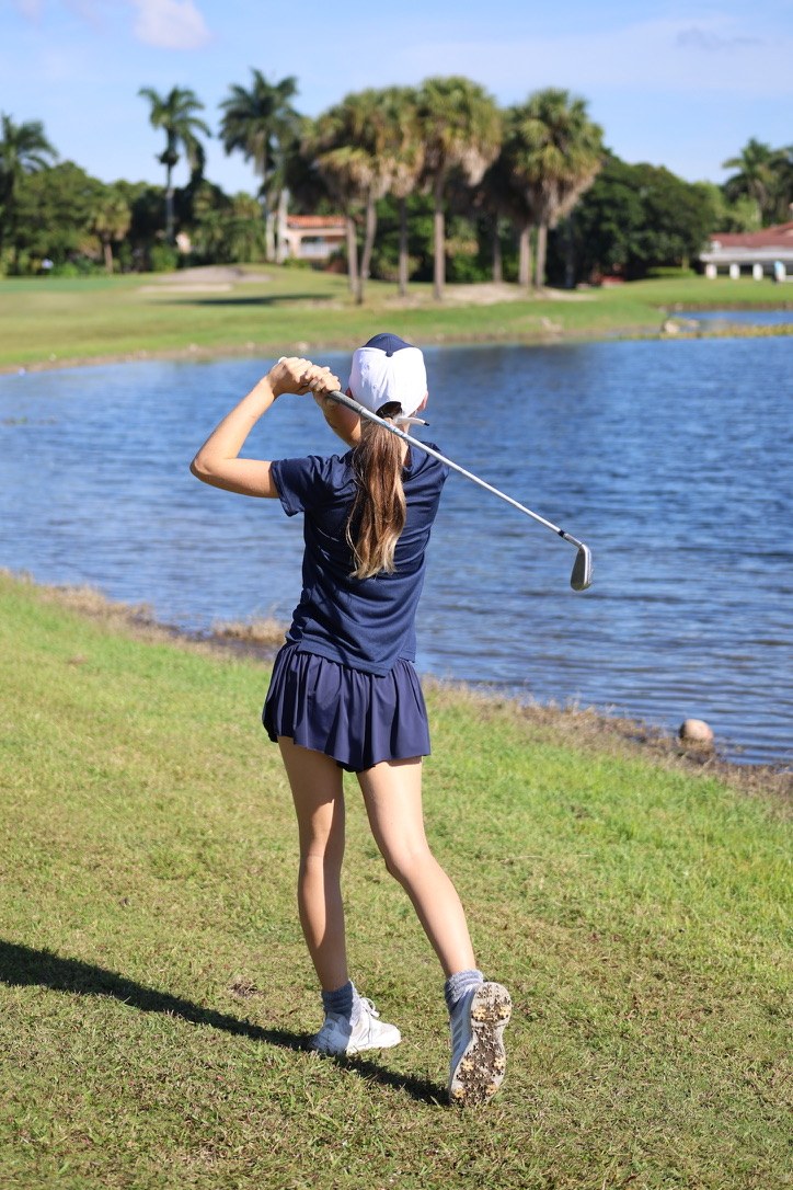 Golfer in navy holding her finish beside a lake