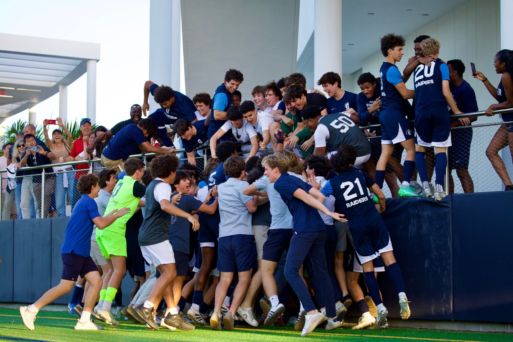 Gulliver Raiders boys soccer players and fans celebrating together at the wall of the stands